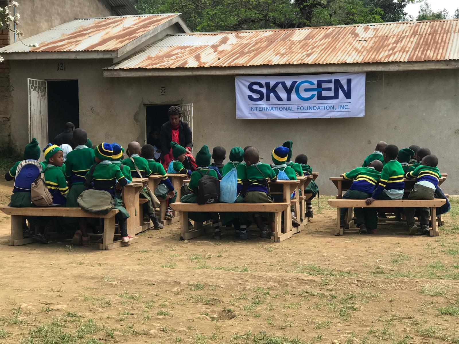 Schoolchildren seated on wooden benches during an outdoor preventative-health outreach session